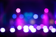 Defocus Blurred Abstract Purple Bokeh Background. Rock Concert Performing On Stage With Musician With Purple Light On Dark Background. Blurry Music Performance In Rock Band Concert. Out Of Focus