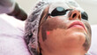 © ALEXEY - A woman in protective glasses with smeared black mask on her face is undergoing a procedure in a beauty salon.