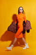 Fashion asian female model. Orange dress, down jacket, white boots, sunglasses.