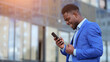 © lenblr - African American man happy winning tender for business after upgrading startup. Mature businessman looks for excellent results on smartphone with smile, sunlight