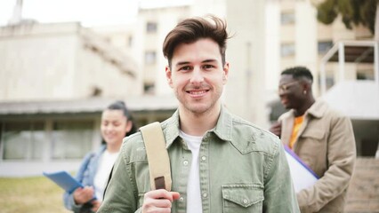 Wall Mural - Awesome attractive male student smiling and looking at camera standing with success attitude at the university campus. At the background three teenagers walking and talking. Education concept. High