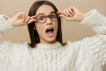 A Funny, Emotional Woman Stands On A Light Background In A Large White Sweater, Wearing Glasses Slightly Lowered, Holding Them With Both Hands And Menacingly Looking Around With Her Elbows Apart