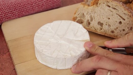 Sticker - mains d'un homme coupant du camembert. Pain sur planche de bois