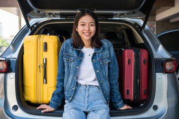 Smiling Asian young girl sit on suv car trunk with suitcases