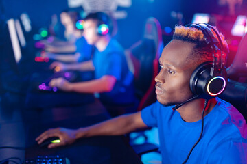 Wall Mural - Closeup portrait african young man in headphones. Team professional gamer playing winning tournaments online games computer, neon colours, soft focus