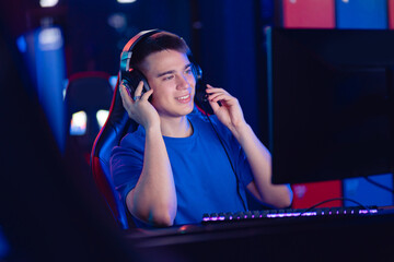Wall Mural - Happy Young caucasian man pro gamer streamer say in microphone in online video game, neon color soft focus. Concept esport tournament
