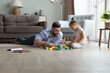 Happy cheerful dad and cute little daughter girl playing toy blocks on heating floor, enjoying learning game, arranging cubes from heap. Young father entertaining kid at home