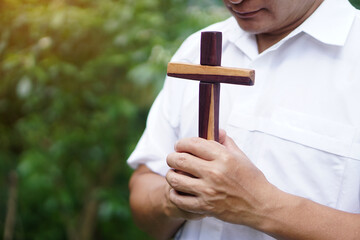 Closeup wooden cross that held by Asian man in white shirt. Concept : Christian worship.  Faith, forgiveness,belief, love and hope. Religious symbol of Christianity.      