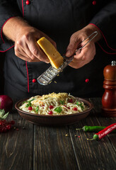 The cook adds hard cheese to spaghetti with spices in a plate. Menu or recipe for a delicious lunch for a hotel or restaurant.