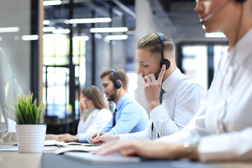 Wall Mural - Portrait of call center worker accompanied by his team. Smiling customer support operator at work.