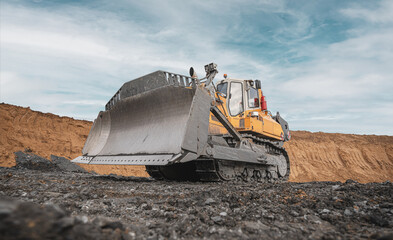 Yellow excavator in career moves overburden. Bulldozer combs the ground, with the bright sun and nice blue sky in the background