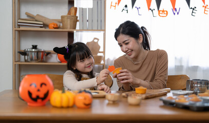 Happy smiling family mother and daughter making Halloween home decorations together while sitting at wooden table.