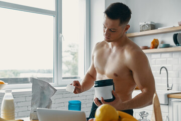 Wall Mural - Confident fit man preparing protein drink while standing at the kitchen