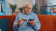 © Andrii Iemelianenko - Happy shopaholic consumer senior old grandfather man sitting at home making online order food delivery, payment with credit plastic bank card. Discount sale on internet. Elderly retired pensioner guy