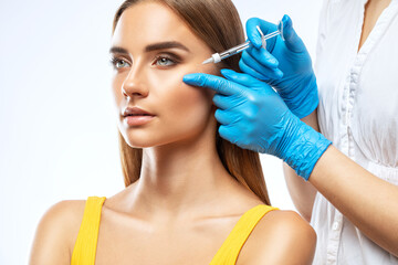 Cosmetologist makes rejuvenating anti wrinkle injections on the face of a beautiful woman in a yellow blouse. Female aesthetic cosmetology in a beauty salon.