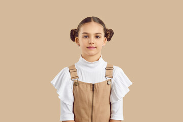 Studio portrait on beige background of beautiful cute preteen girl with hairstyle with two bundles. Caucasian kid girl in fashionable teenage clothes looks at camera with faint smile. Banner.