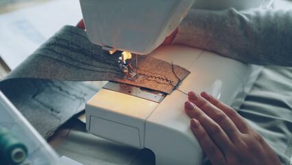 Wall Mural - Close-up view of modern electric sewing machine working stitching piece of fabric. Young girl's manicured hand and colorful sewing threads are visible.