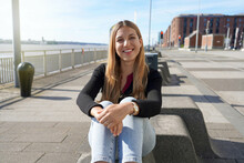 Young Beautiful Woman Sitting Relaxed On Liverpool Waterfront On Sunny Day, England