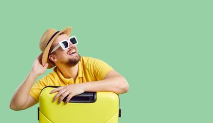 Wide narrow shot of funny smiling young man in summer hat and sunglasses with suitcases dream of vacation or trip. Happy male traveler imagine good holidays. Copy space. Travel and tourism concept.