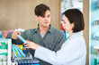 © DJ Creative Studio - PAsian pharmacist advising patient caucasian customer about healthcare product and medicine instructions in pharmacy.