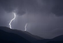 Dark, Stormy Night In The Mountains With Violent Lightning Striking The Peaks Under A Cloudy Sky