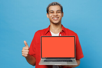 Wall Mural - Young IT man of African American ethnicity 20s he wear red shirt hold use work on laptop pc computer with blank screen workspace area show thumb up isolated on plain pastel light blue cyan background.