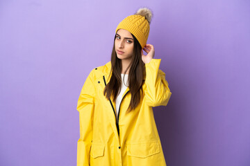 Wall Mural - Young caucasian woman wearing a rainproof coat isolated on purple background having doubts