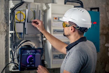 Wall Mural - Man, an electrical technician working in a switchboard with fuses, uses a tablet.