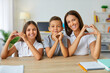 © Studio Romantic - Happy Caucasian children and woman mother or teacher show heart gesture rejoicing at beginning of school year and receiving quality primary education sits in classroom at desk. Back to school