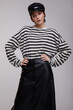 © SBekhinov - High fashion photo of a beautiful elegant young woman in a pretty black long leather skirt, black and white striped sweater with sleeves, hat posing over white, soft gray background. Studio Shot.
