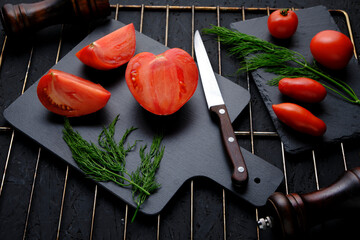 sliced tomatoes slate, dill greens, two spice mills and knife with wooden handle on grill.