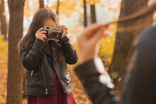 Child Girl Photographer Takes Pictures Of A Mother In The Park In Autumn. Hobbies, Photo Art And Leisure Concept.