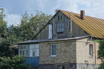 Sticker - one old rural brown brick house with a wooden attic under a rusty iron roof on the street against the sky