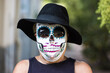 Portrait of an elderly lady with a catrina mask and hat, celebrating Halloween and All Souls' Day, on the street. Celebration, costume, party and mask concept.