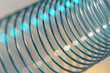 Closeup of coiled metal spring with sufficiently high strength and elastic properties in neon blue light over bright background. Macro photo, shallow depth of field