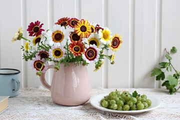 Summer still life with a bouquet in a pink jug and green gooseberries on a plate.