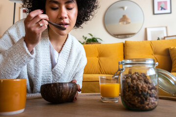 African American woman eating granola for breakfast at home living room. Coffee and orange juice, Copy space.