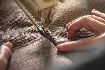 Wall Mural - Women's hands in the process of sewing on professional equipment. Sewing fabric in production. Close-up