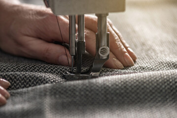 Wall Mural - Women's hands in the process of sewing on professional equipment. Sewing fabric in production. Close-up