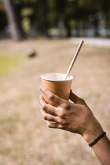 Disposable paper cup with a drinking straw in the hand of a teenager in the park on a warm day