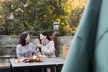 Asian girlfriends having fun together with maple leaves outdoor. Friendship concept with happy girls at autumn city vacation. Millennial lifestyle with female best friends women at fall season in