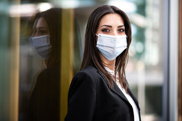 Wall Mural - Confident young female manager outdoor in a modern urban setting and wearing a protective mask against covid 19 coronavirus pandemic