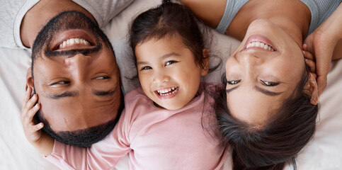 Poster - Happy family with child on bed in a face portrait for interracial love, care and happiness together. Girl kid from Mexico with mother and father or parents relaxing at home and bonding from above