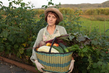 Smiling Senior Woman With Basket Of Freshly Picked Vegetables Standing By Plant