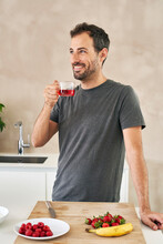 Smiling Man With Tea Cup Standing By Fruits In Kitchen