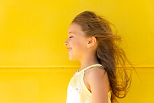 Happy Girl With Long Hair Standing In Front Of Yellow Wall