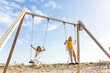 © Westend61 - Cheerful girl with brother playing on swing at beach