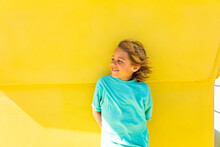 Smiling Boy Standing In Front Of Yellow Wall On Sunny Day
