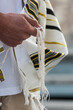 Closeup of a Jewish man praying while holding the strings or tzit-tzit on his tallit in his hand and reciting the shema yisrael prayer.
