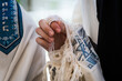 Closeup of a Jewish man praying while holding the strings or tzit-tzit on his tallit in his hand and reciting the shema yisrael.